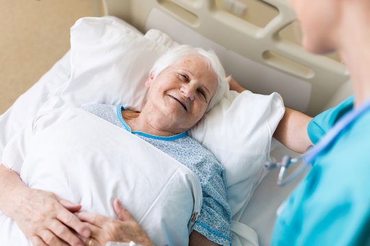 Nurse caring for a smiling elderly patient in a hospital bed
